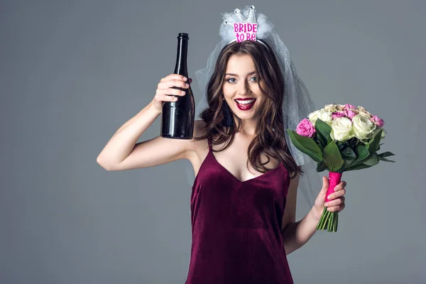 Smiling future bride in veil for bachelorette party with bouquet and champagne looking at camera isolated on grey — Stock Image Smiling Future Bride Veil Bachelorette Party Bouquet Champagne Looking Camera Stock Image