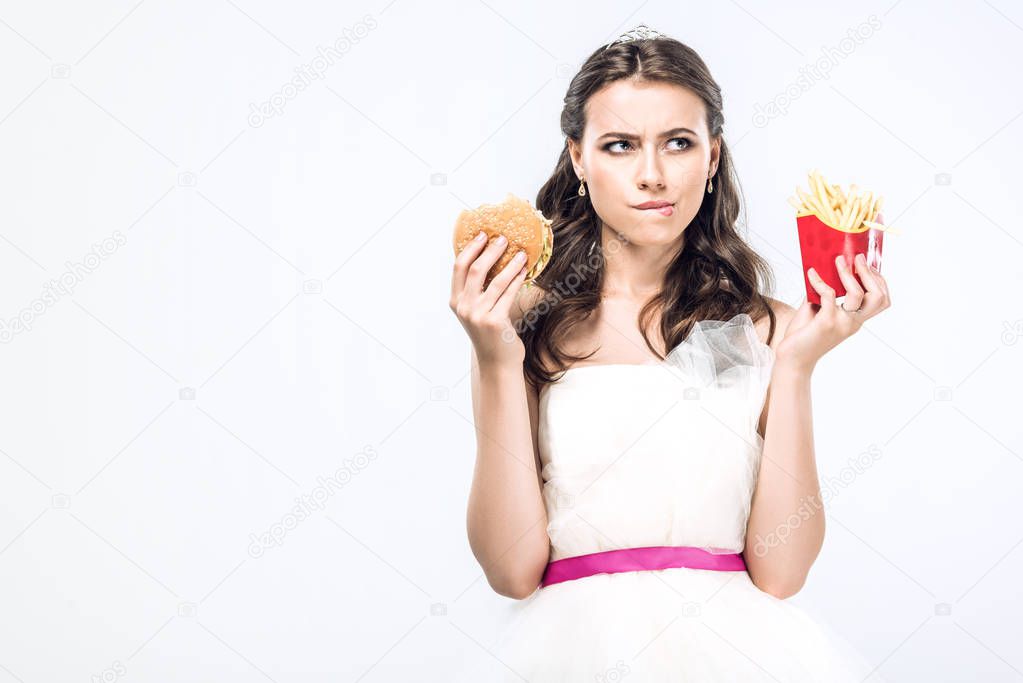 thoughtful young bride in wedding dress with burger and french fries looking up isolated on white