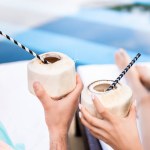 Gedeeltelijke weergave van paar ontspannen met cocktails van de kokosnoot met rietjes in de buurt van zwembad