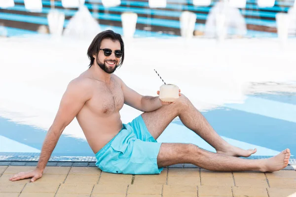 handsome bearded man with green coconut cocktail sitting at poolside