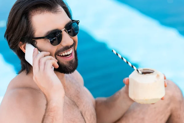 Uomo Sorridente Con Cocktail Cocco Che Parla Smartphone Bordo Piscina — Foto stock gratuita