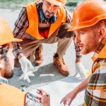 Nahaufnahme einer Gruppe von Bauarbeitern mit harten Hüten, die sich über Baupläne unterhalten