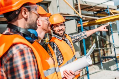 close-up shot of group of equipped builders looking away at construction site clipart