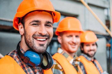close-up shot of group of equipped builders looking at camera at construction site clipart