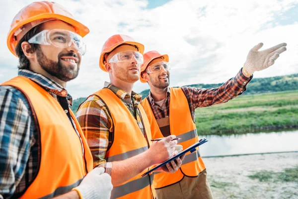 Grupo Construtores Chapéus Duros Coletes Reflexivos Apontando Algum Lugar — Fotografia de Stock