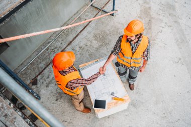 high angle view of builders shaking hands at construction site clipart