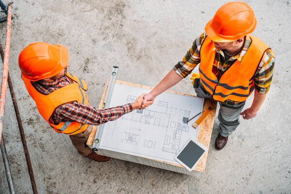 high angle view of builders shaking hands over blueprint at construction site