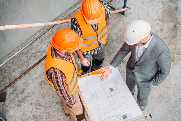 high angle view of builders and architect discussing blueprint at construction site