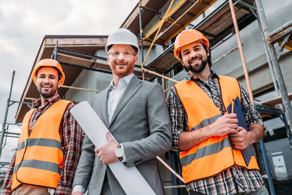 вид снизу на строителей и архитектора с чертежом, смотрящим в камеру
