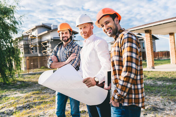 группа архитекторов с чертежами в саду на строительной площадке
