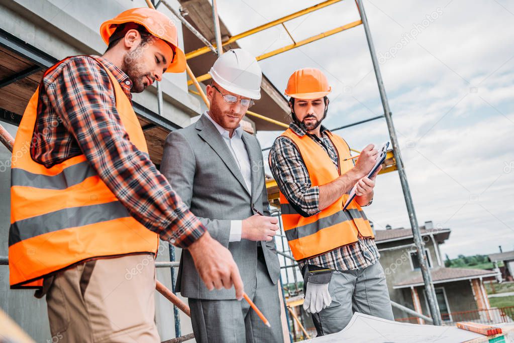 bottom view of builders and architect discussing blueprint at construction site