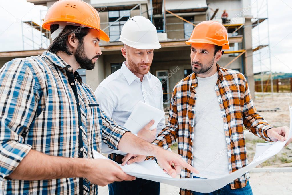 group of architects with building plan having conversation in front of construction site