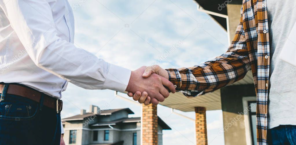 cropped shot of architects shaking hands in front of construction site