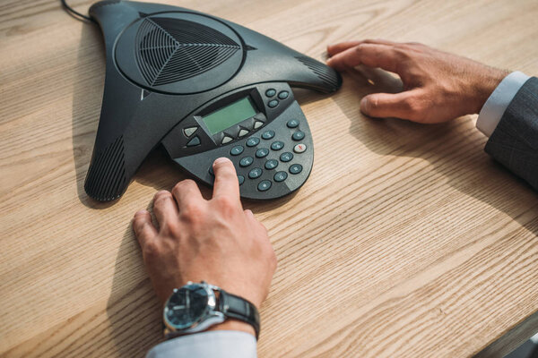 cropped shot of businessman with stylish wristwatch using speakerphone at workplace