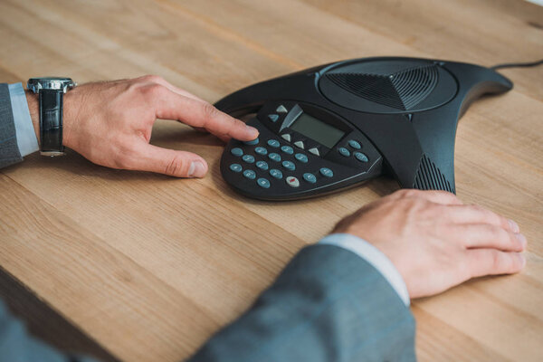 cropped shot of businessman using conference phone at workplace