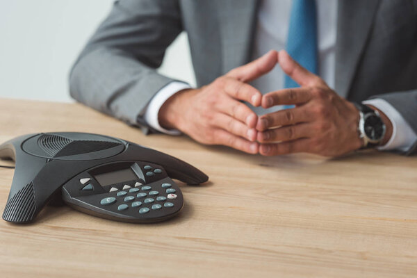 cropped shot of businessman sitting in front of speakerphone and having conversation at office