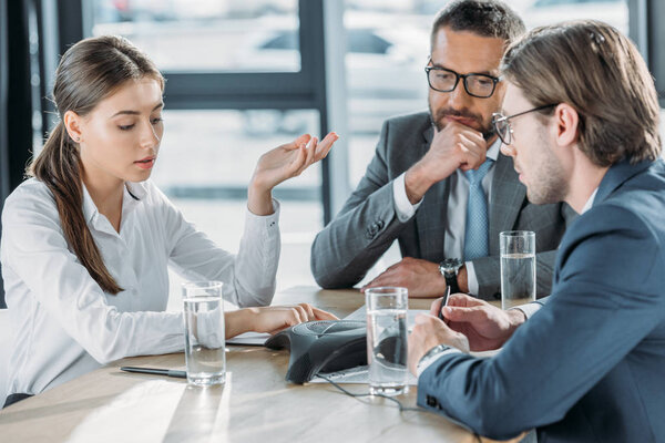 confident business people sitting around conference phone at modern office