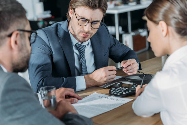 серьезные деловые люди сидят вокруг конференц-телефона в современном офисе
