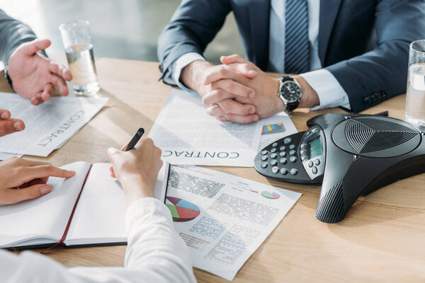 обрезанный снимок деловых людей, беседующих с документами и громкоговорителем на столе в современном офисе
