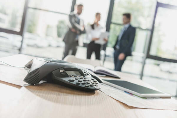 close-up shot of conference phone with blurred business people on background at modern office