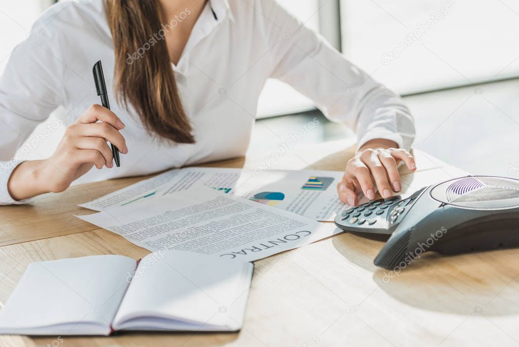 cropped shot of businesswoman with paperwork using conference phone at office