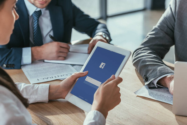 обрезанный снимок предпринимательницы, держащей планшет с приложением facebook на экране во время встречи
