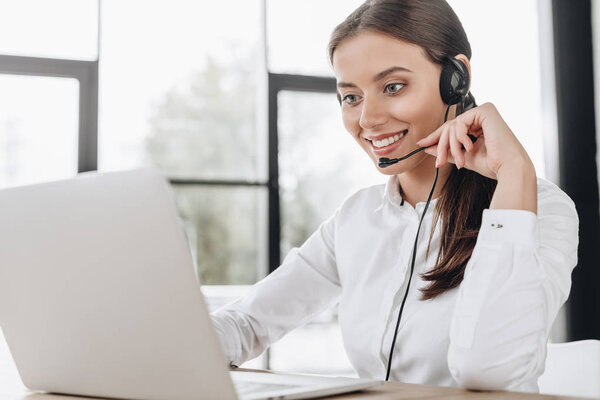 beautiful female call center worker with headphones and laptop sitting at workplace