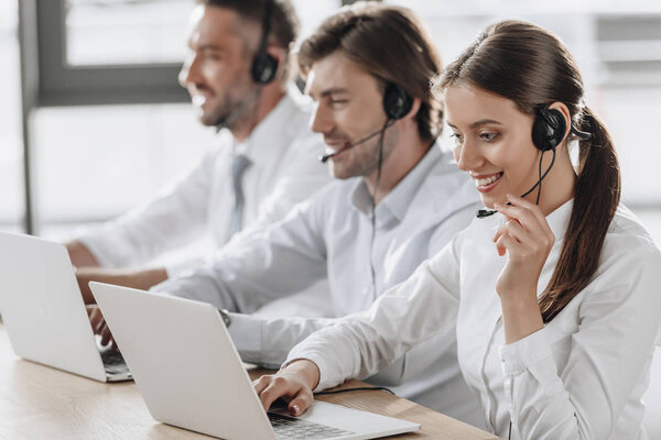 smiling call center managers in white shirts working together while sitting in row at modern office