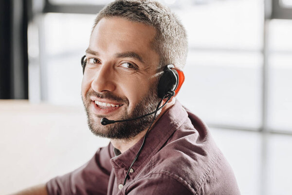 handsome smiling call center worker in headphones with microphone looking at camera