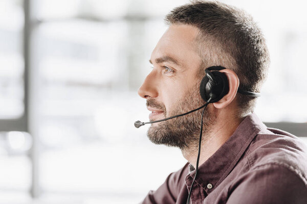 side view of handsome call center worker in headphones with microphone