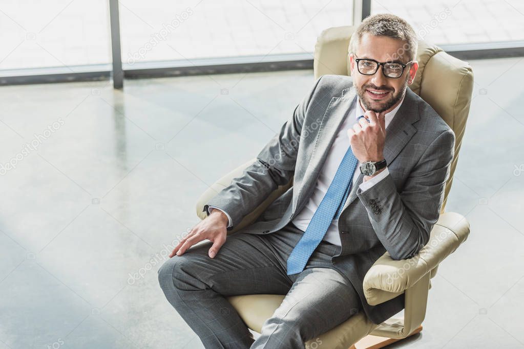 high angle view of handsome smiling businessman sitting on luxury armchair at modern office