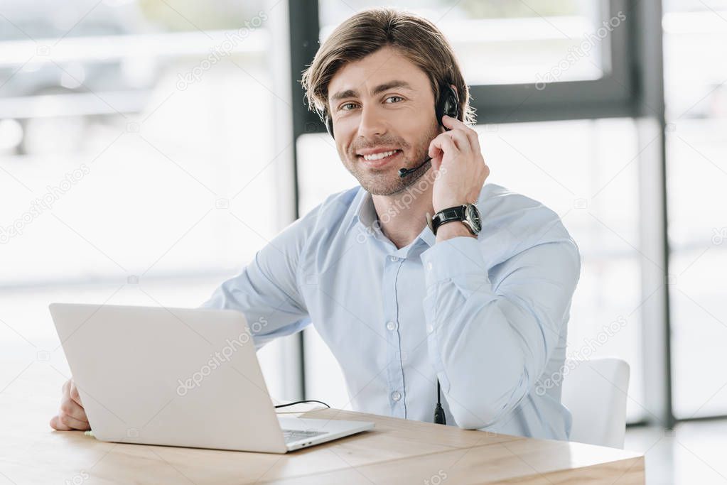 smiling call center worker with laptop looking at camera while sitting at workplace