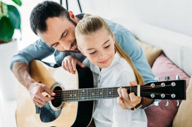 happy father and daughter playing guitar together at home