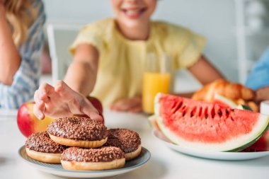 cropped shot of smiling child reaching for donut during dinner clipart