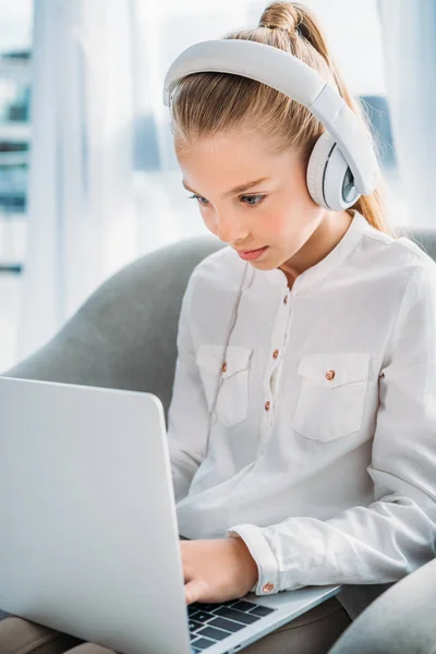 Klein Kind Geconcentreerd Hoofdtelefoons Met Behulp Van Laptop Zittend Leunstoel — Gratis stockfoto