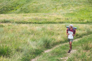 Gezgin harita tutarak ve yaz çayır yolda yürüyen sırt çantası ile