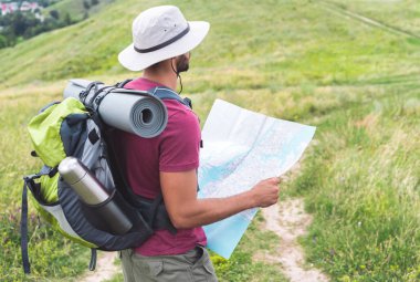 male hiker in hat with backpack, thermos, tourist mat and map  