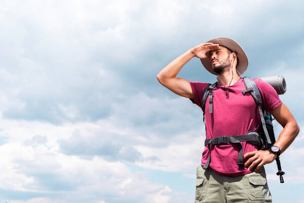 handsome tourist in hat looking away, with cloudy sky background