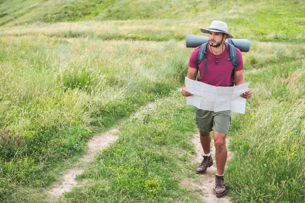 徒步旅行者在帽子与背包持有地图和走在路径上 — 图库照片