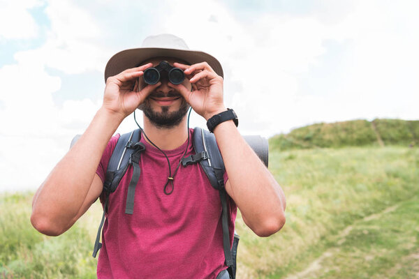 male tourist in hat with backpack looking in binoculars