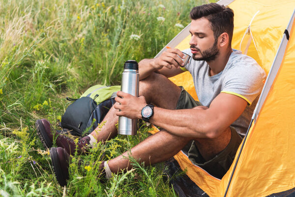 tourist sitting in yellow tent and drinking coffee from thermos
