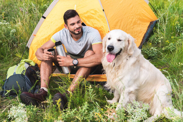 traveler with thermos sitting in tent and looking at dog