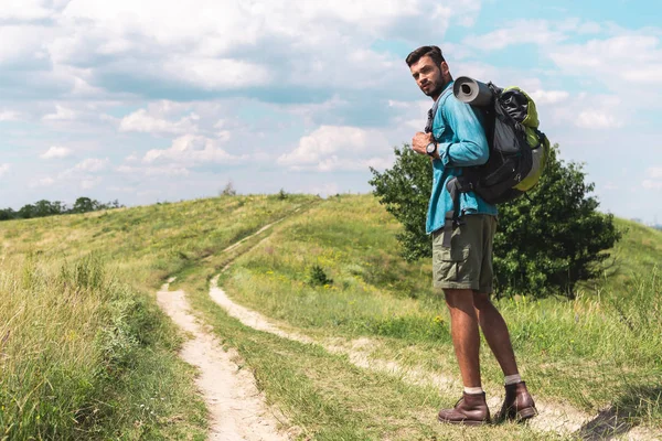 英俊的徒步旅行者与背包步行在绿色草甸 — 图库照片