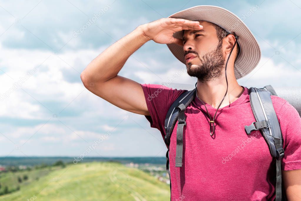 traveler in hat with backpack looking away on summer meadow