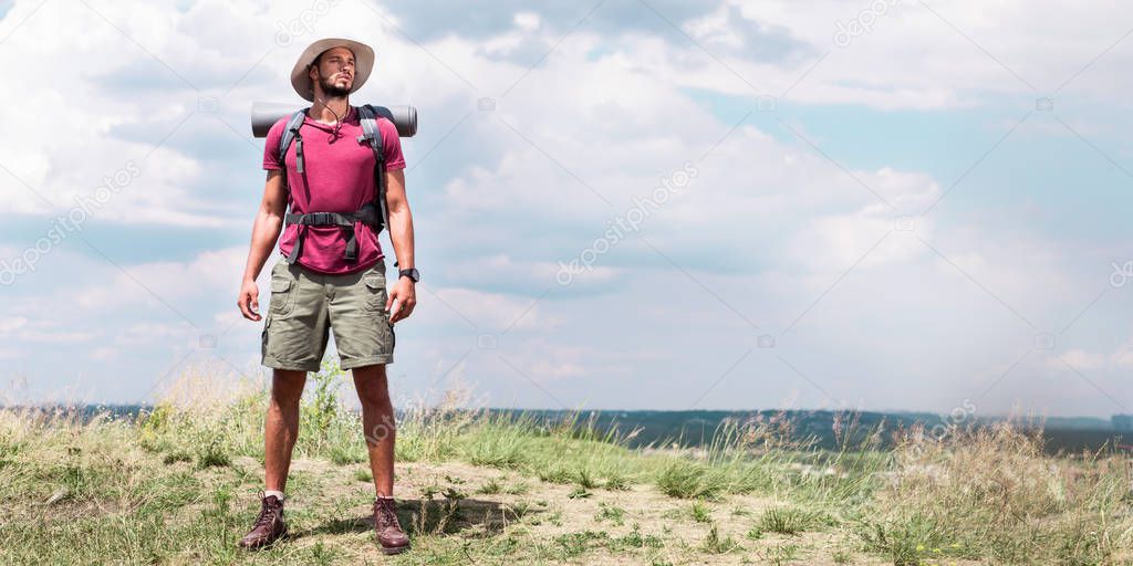 handsome traveler with backpack standing at summer meadow