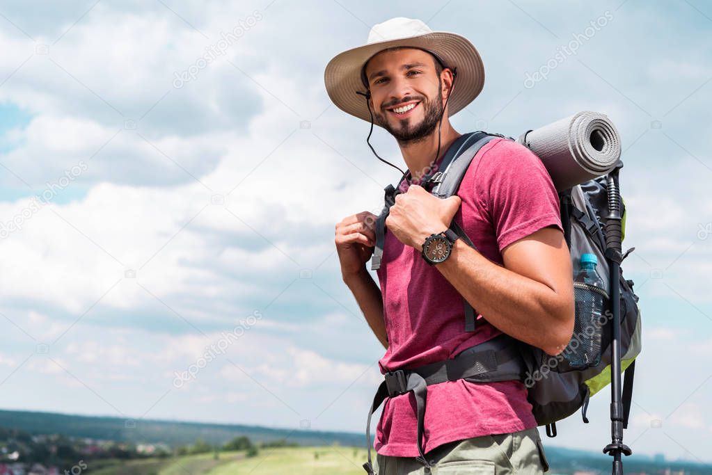smiling traveler in hat with backpack and tourist mat looking at camera