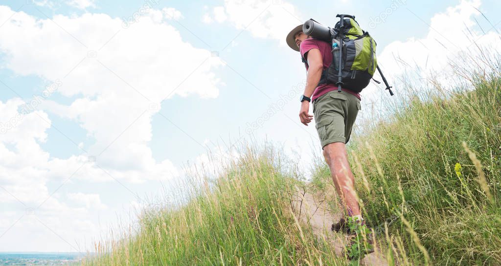 male hiker in hat with backpack and tourist mat walking on path