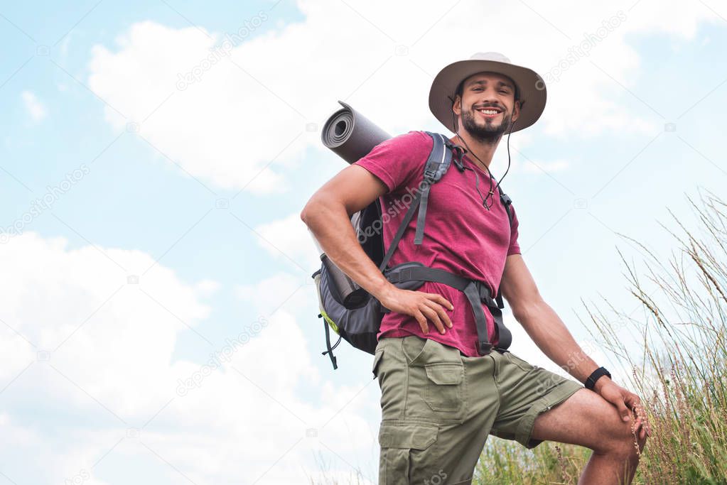 smiling hiker in hat with backpack and tourist mat