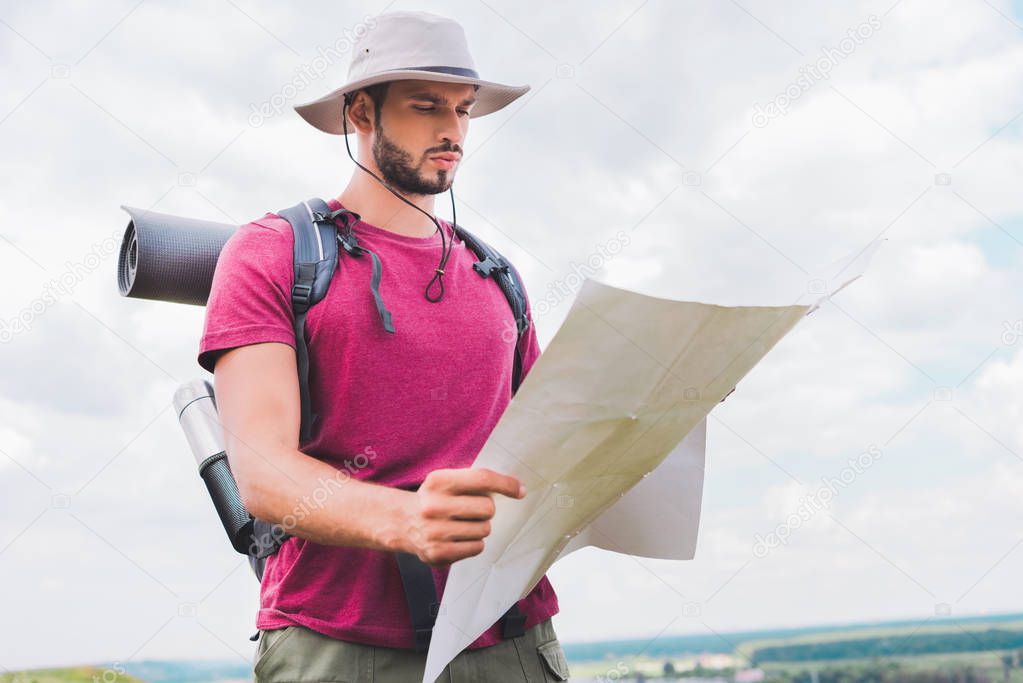 handsome hiker in hat with backpack looking at map