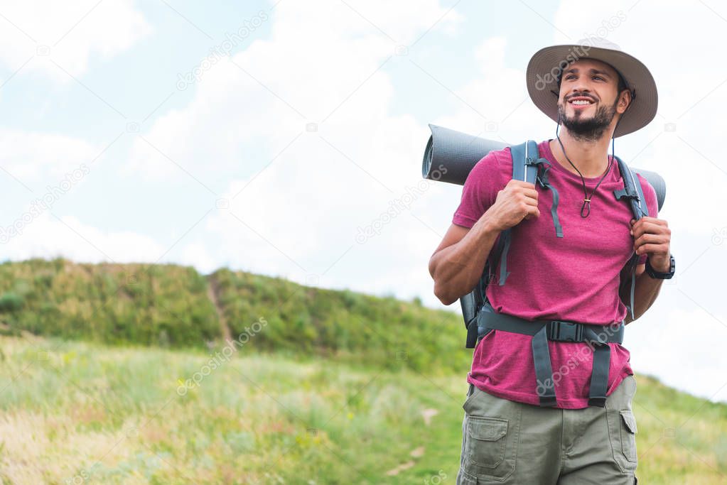 happy hiker with backpack walking on green meadow